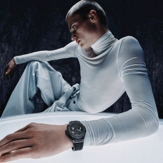 Junger Mann in futuristischem Setting mit heller Kleidung präsentiert eine Hublot Uhr mit schwarzem Gehäuse und Armband.