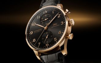 IWC Portugieser Chronograph in Rotgold mit schwarzem Zifferblatt und schwarzem Lederarmband vor schwarz-braunem Hintergrund