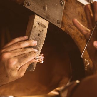 Goldschmied sitzt an der Werkbank und bearbeitet einem Farbsteinring