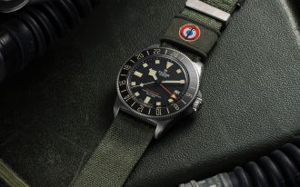 TUDOR Pelagos FXD GMT Uhr in Titan mit schwarzer Luenette, schwarzem Zifferblatt und militarygruenem Textilband auf militarygruenem Hitnergrund liegend