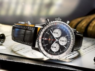 Breitling Navitimer Chronograph in Stahl mit schwarz-silbernem Pandazifferblatt und schwarzem Lederarmband seitlich auf Flugunterlagen liegend