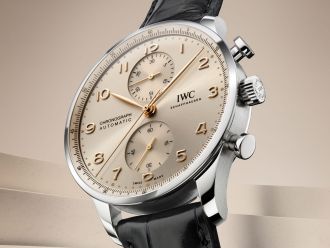 Portugieser Chronograph in Stahl mit sandfarbenem Zifferblatt und Schwarzem Lederarmband vor sandfarbenem Hintergrund