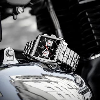 TAG Heuer Monaco Chronograph in Stahl mit schwarzem Lederarmband seitlich auf einem Motorrad liegend