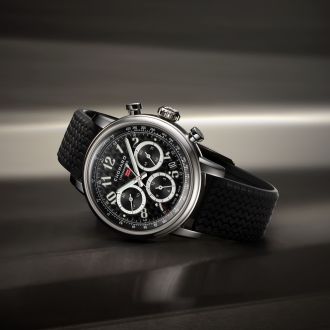 Chopard Mille Miglia Chronograph mit Gehaeuse aus Stahl, schwarzem Zifferblatt mit arabischen Ziffern und schwarzem Kautschukarmband seiltich liegend vor dunklem Hintergrund