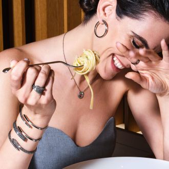 Weibliches Model isst Spaghetti und traegt dabei mehrere Armreifen, einen Ring, eine Halskette mit Anhaenger und Creolen aus der Like Kollektion von Crivelli