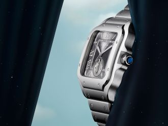 Cartier Santos Uhr komlett in Stahl mit anthrazitgrauem Zifferblatt seitlich vor blauem Himmel und dunkelblauen Vorhaengen links und rechts im Bild