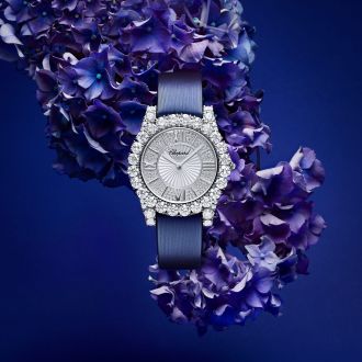 Chopard L'Heure du Diamant Damenuhr mit Gehaeuse in Weissgold besetzt mit Diamanten, silbernem Zifferblatt mit roemischen Ziffern und blauem Textilarmband vor blauem Hintergrund