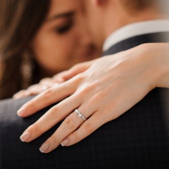 Hand mit elegantem Verlobungsring aus Weißgold mit Diamant, getragen von einer Frau in inniger Umarmung – Symbol für Liebe und Verlobung bei Juwelier Mühlbacher.