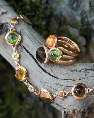 Drei Bouton Ringe von Tamara Comolli in Rosegold mit je einem Farbstein in orange, gruen und braun und dazu passendes Bouton-Armband auf Holzast drapiert