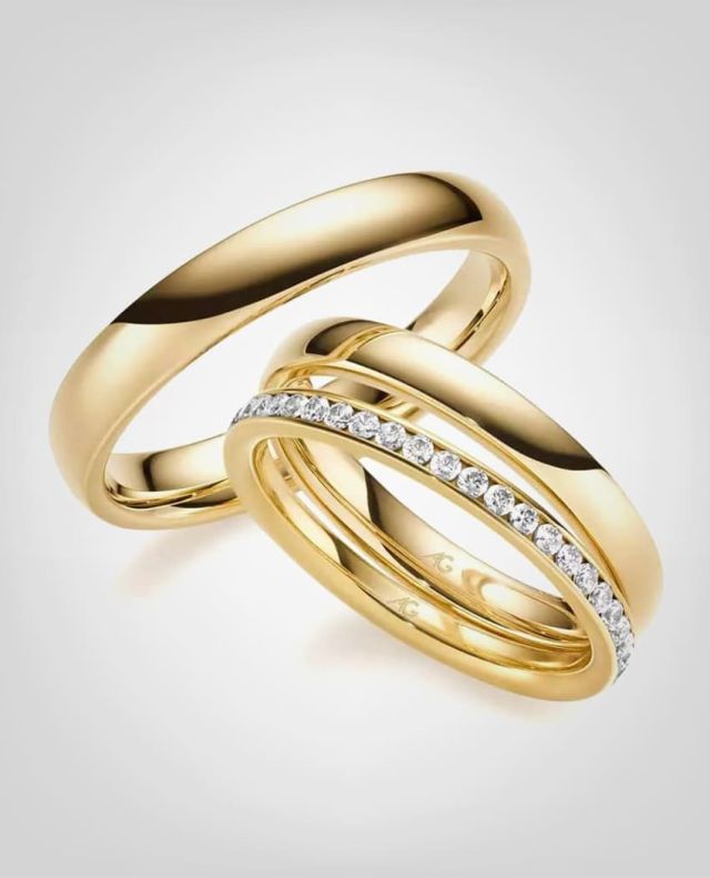 Eheringe von August Gerstner in Gelbgold mit einem Vorsteckring in Gelbgold mit Diamanten vor einem grauem Hintergrund