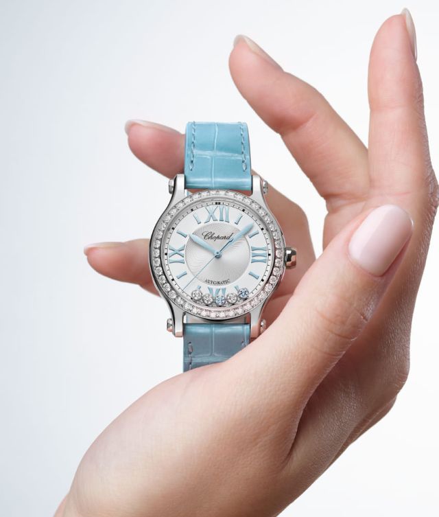 Chopard Happy Sport Damenuhr mit Gehaeuse in Stahl mit Diamantluenette, silbernem Zifferblatt mit 5 beweglichen Diamanten und hellblauem Lederarmband stehend auf einer Hand