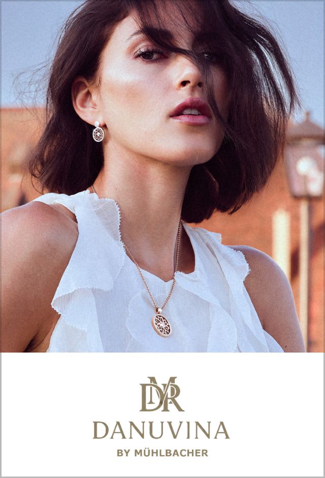 Model mit kurzem, dunklem Haar trägt goldene Ohrringe und eine passende Halskette mit filigranem Anhänger aus der Schmuckkollektion DANUVINA by Mühlbacher.