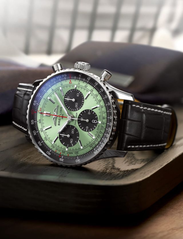 Breitling Navitimer Chronograph in Stahl mit mintgruenem Zifferblatt und schwarzem Lederarmband seitlich liegend auf Lifestylehintergrund