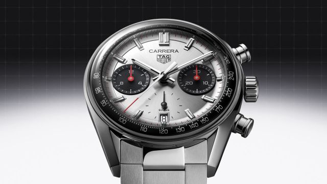 TAG Heuer Carrera Chronograph mit Stahlgehaeuse, silber-schwarzem Zifferblatt und Stahlarmband vor schwarz-grauem Hintergrund