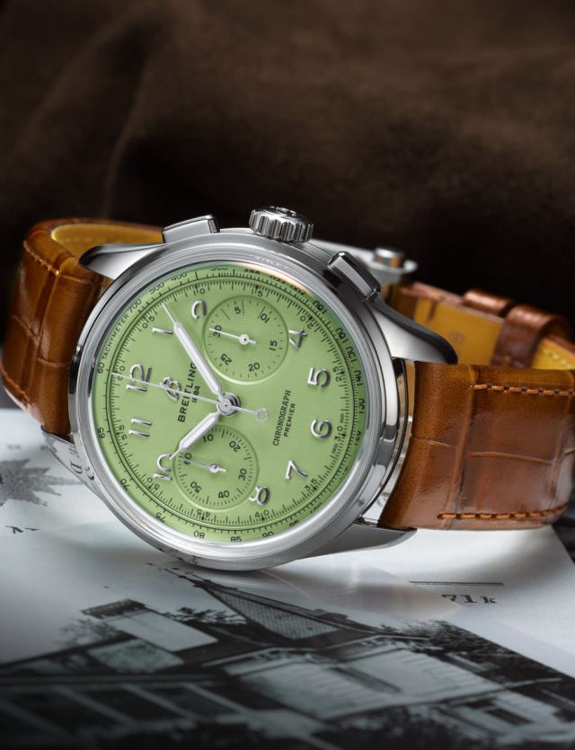 Breitling Premier Chronograph in Stahl mit pistaziengruenem Zifferblatt und cognacbraunem Lederband seitlich liegend auf Lifestylehintergrund