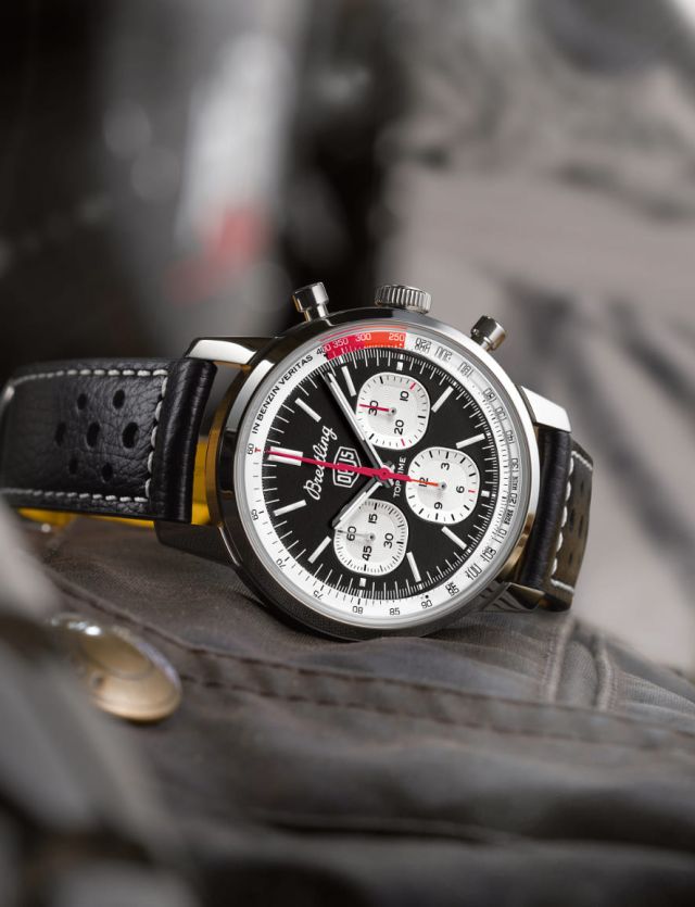 Breitling Top Time Chronograph in Stahl mit schwarzem Zifferblatt, silbernen Totalisatoren un schwarzem Lederarmband seitlich liegend auf Lifestylehintergrund