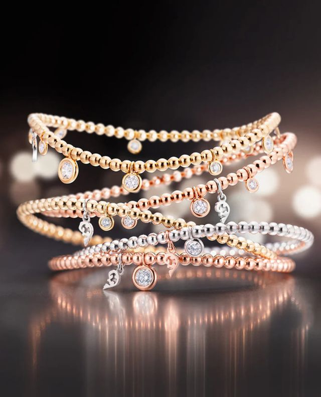 Capolavoro Prosecco Armbaender in Gelb-, ROse- und Weissgold mit Diamantanhängern auf grauem Hintergrund