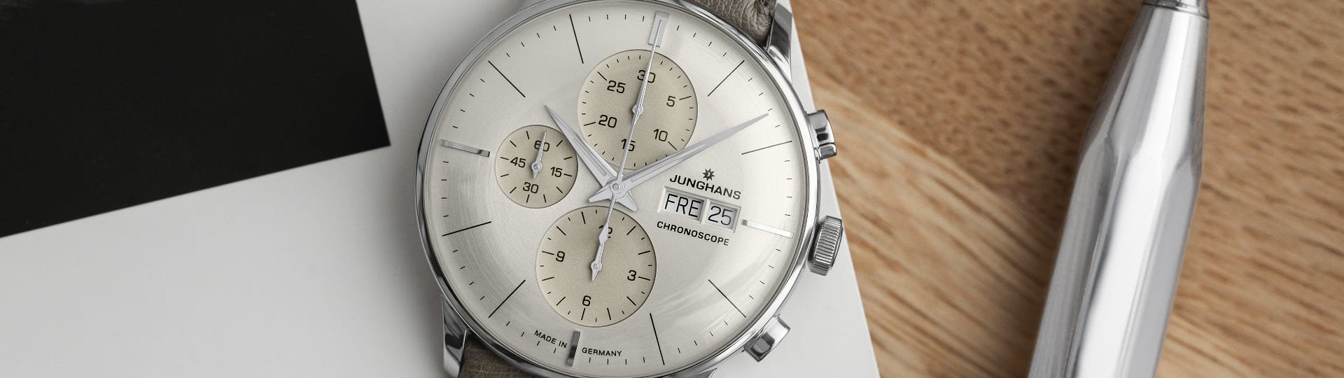 Junghans Meister Chronograph in Stahl mit silbergrauem Zifferblatt und taupefarbenem Lederarmband auf Schreibtisch liegend