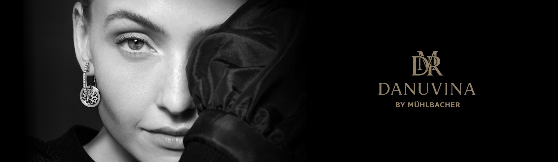 Elegante Frau mit Ohrringen von Danuvina by Mühlbacher, in monochromem Porträt vor dunklem Hintergrund, mit luxuriösem, minimalistischen Markenlogo rechts im Bild.