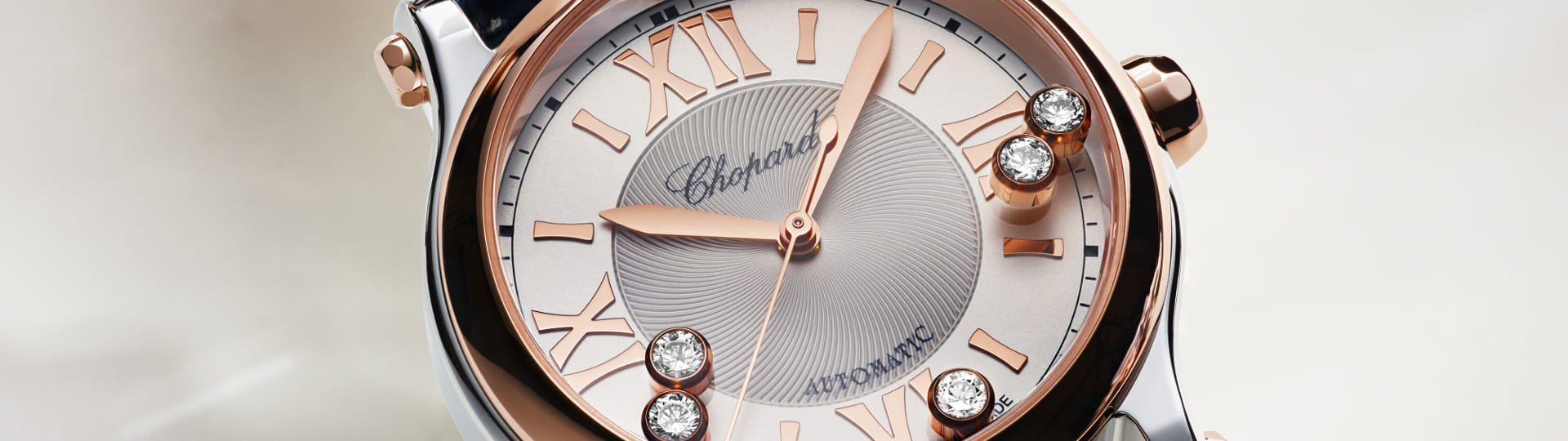 Chopard Happy Sport Damenuhr mit Gehaeuse in Stahl, Krone und Luenette in Rosegold, silbernem Zifferblatt mit roemischen Ziffern und 5 beweglichen Diamanten vor beigefarbenem Hintergrund