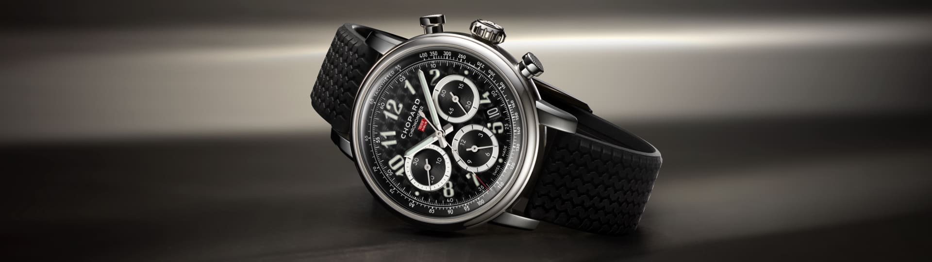 Chopard Mille Miglia Chronograph mit Gehaeuse aus Stahl, schwarzem Zifferblatt mit arabischen Ziffern und schwarzem Kautschukarmband seiltich liegend vor dunklem Hintergrund