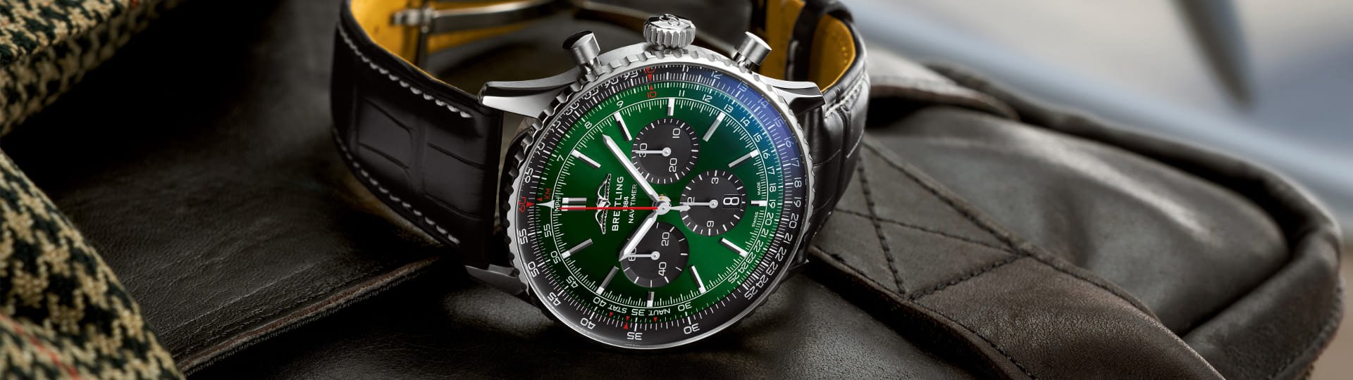 Breitling Navitimer Chronograph in Stahl mit gruenem Zifferblatt, schwarzen Totalisatoren und schwarzem Lederarmband seitlich auf Lifestylehintergrund liegend