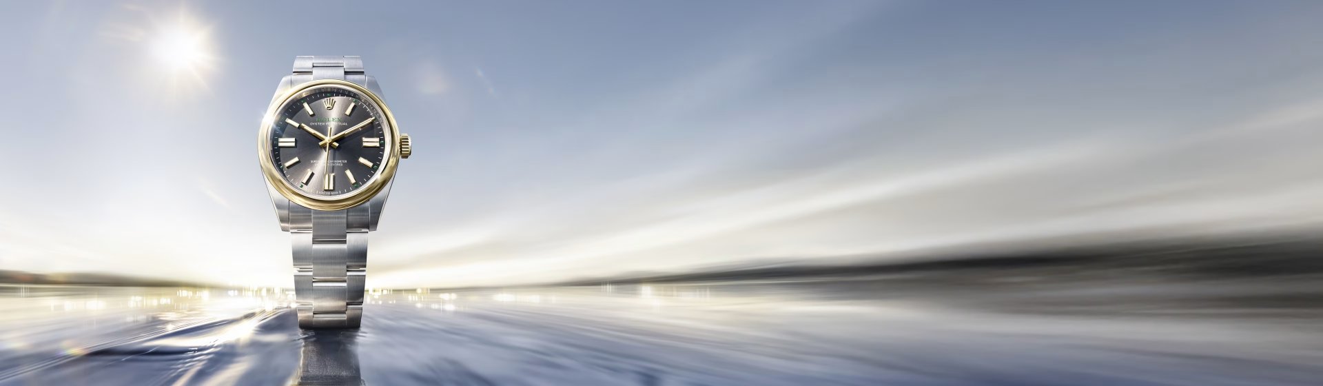 Rolex Oyster Perpetual Armbanduhr in Edelstahl und Gold mit grauem Zifferblatt vor dynamischem, lichtdurchflutetem Hintergrund