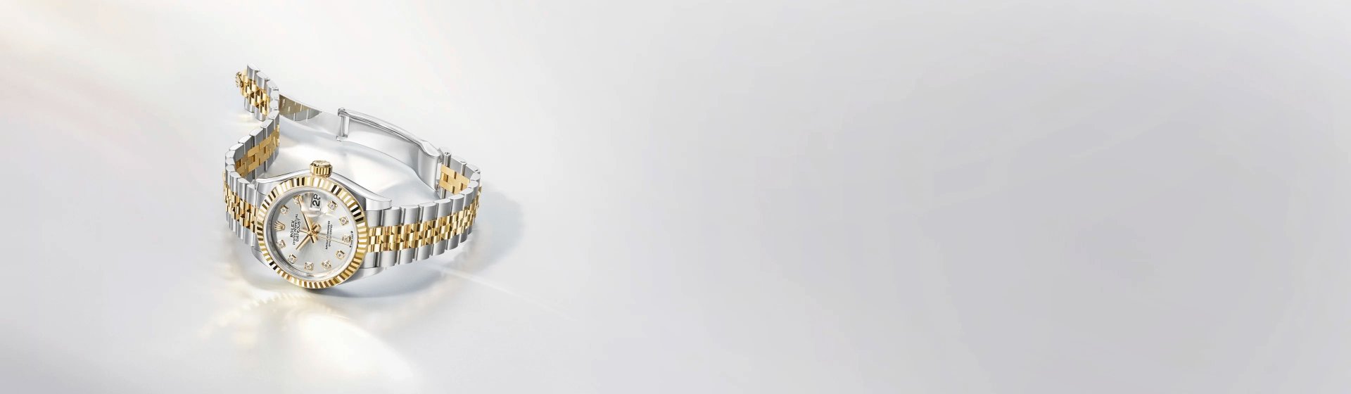 Rolex Lady Datejust in Stahl-Gold mit Perlmuttzifferblatt und geriffelter Lünette seitlich auf hellgrauem Hintergrund liegend