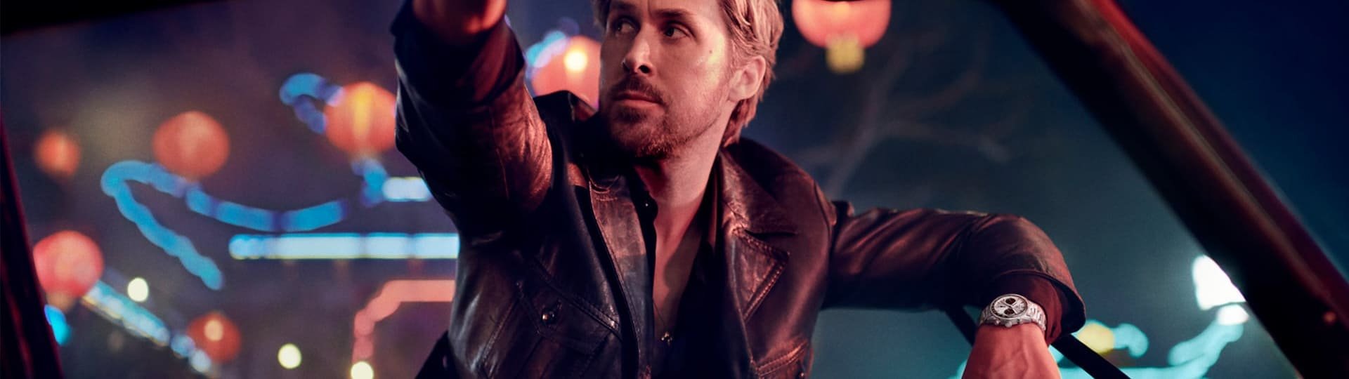 Ryan Gosling an einer Autotuer lehnend traegt am Handgelenk einen Carrera Chronographen von TAG Heuer in Stahl mit silberschwarzem Panda-Zifferblatt