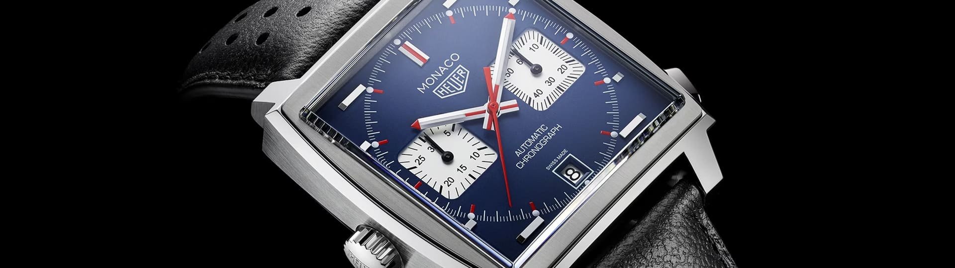 TAG Heuer Monaco Uhr in Stahl mit blauem Zifferblatt, silbernen Totalisatoren und schwarzem Lederarmband mit Lochmuster vor schwarzem Hintergrund