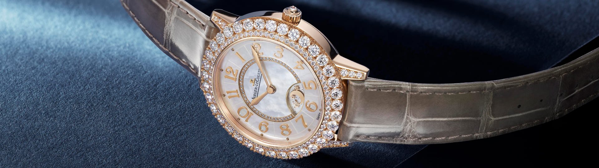 Jaeger-LeCoultre Rendez-Vous Damenuhr in Rosegold mit Diamantluenette, weissem Perlmuttzifferblatt und braunem Lederarmband auf blauem Untergrund liegend