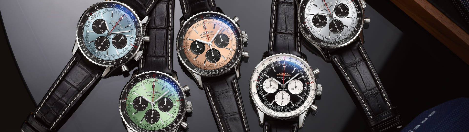 Fuenf Breitling Navitimer Chronographen mit Stahlgehaeuse, unterschiedlich farbigen Zifferblaetter und schwarzen Lederarmbaender auf Lifestylehintergrund