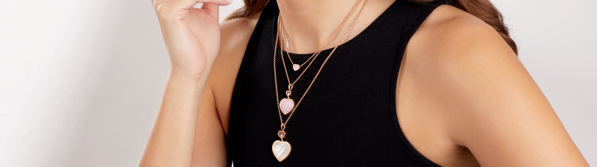 Weibliches Model mit drei Anhaenger aus der Happy Hearts Kollektion an Rosegoldhalsketten, oberer und mittlerer Anhaenger mit rosa Opalherz und unterster mit weissem Perlmuttherz