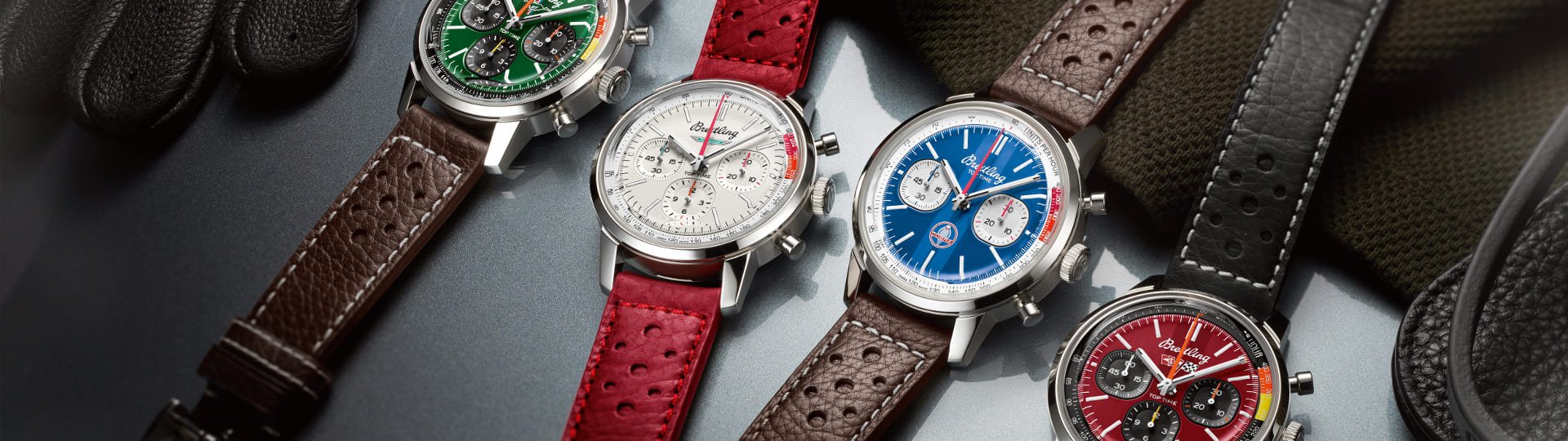 Vier Breitling Top Time Chronographen mit Stahlgehaeusen, unterschiedlich farbigen Zifferblaettern, gruen, weiss, blau und rot und Lederarmbaender liegend auf Lifestylehintergrund