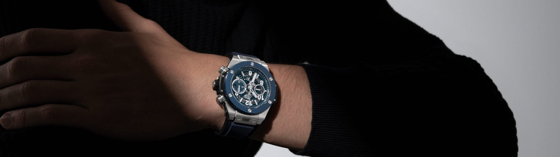 Hublot Big Bang Chronograph am Handgelenk eines Mannes in schwarzem Pullover, Nahaufnahme mit dunklem Hintergrund.
