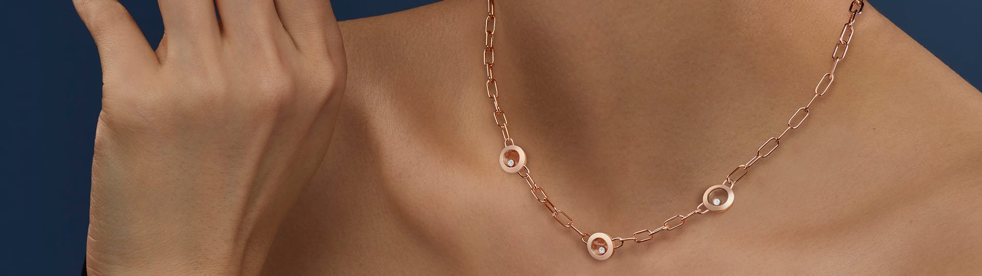 Weibliches Model vor blauem Hintergrun traegt ein Happy Diamonds Collier von Chopard in Rosegold mit drei runden Elementen mit je einem beweglichen Diamanten