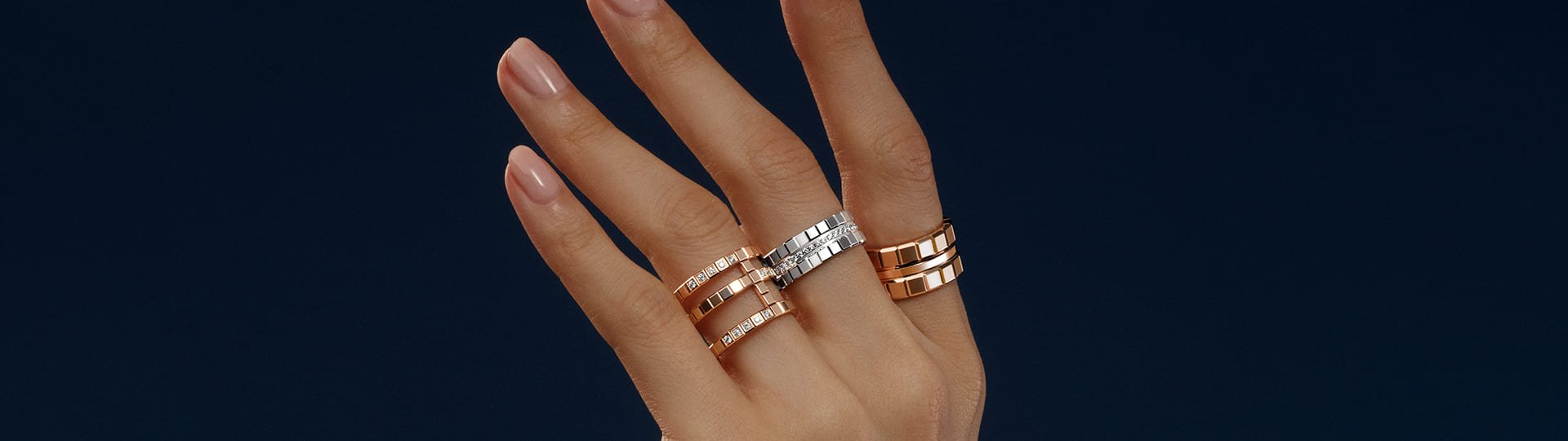 Damenhand vor blauem Hintergrund mit je einem Ice Cube Ring von Chopard an Zeige-, Mittel- und Ringfinger in Rosegold und Weissgold mit Diamanten