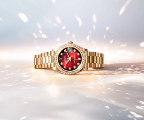 Rolex Datejust aus Gelbgold mit rotem Ombré-Zifferblatt und diamantbesetzter Lünette auf hellem, funkelndem Hintergrund.