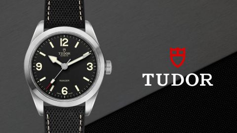 TUDOR Ranger Uhr in Stahl mit schwarzem Zifferblatt auf grau-schwarzem Hintergrund mit TUDOR Logo rechts