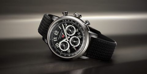 Chopard Mille Miglia Chronograph mit Gehaeuse aus Stahl, schwarzem Zifferblatt mit arabischen Ziffern und schwarzem Kautschukarmband seiltich liegend vor dunklem Hintergrund