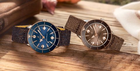 Zwei Superocean Heritage Uhren von Breitling in Stahl und Rotgold mit blauem und braunem Zifferblatt und Luenette und Textilbaendern liegend auf einem Holzuntergrund