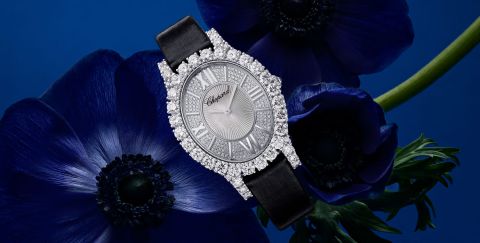 Chopard L'Heure du Diamant Damenuhr mit Gehaeuse in Weissgold besetzt mit Diamanten, silbernem Zifferblatt mit roemischen Ziffern und schwarzem Textilarmband vor blauem Hintergrund