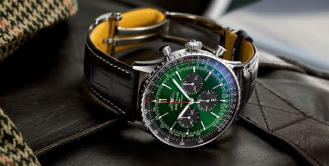 Breitling Navitimer Chronograph in Stahl mit gruenem Zifferblatt, schwarzen Totalisatoren und schwarzem Lederarmband seitlich auf Lifestylehintergrund liegend