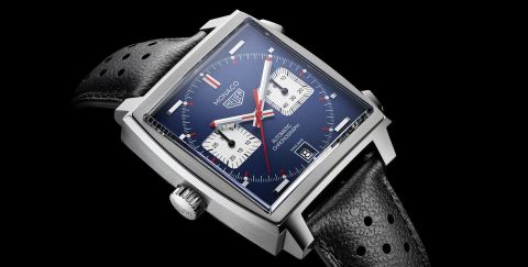 TAG Heuer Monaco Uhr in Stahl mit blauem Zifferblatt, silbernen Totalisatoren und schwarzem Lederarmband mit Lochmuster vor schwarzem Hintergrund