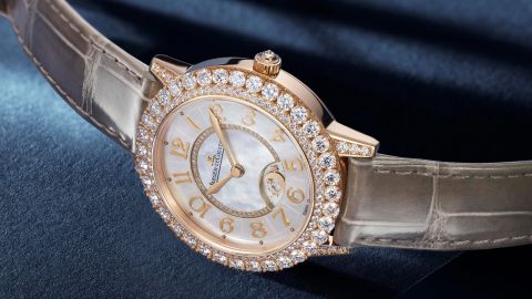 Jaeger-LeCoultre Rendez-Vous Damenuhr in Rosegold mit Diamantluenette, weissem Perlmuttzifferblatt und braunem Lederarmband auf blauem Untergrund liegend