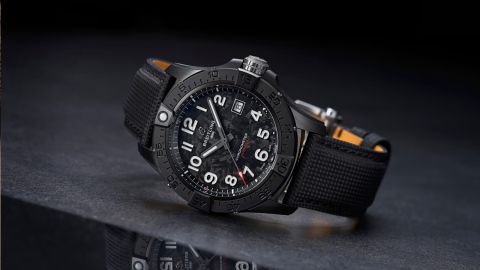 Breitling Avenger Night Mission Uhr mit schwarzem Gehaeuse, Zifferblatt und Textilarmband seitlich auf dunklem Untergrund liegend