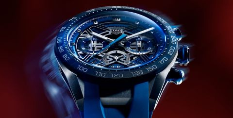 Gehaeuse einer TAG Heuer Carrera Chronograph in Titan mit blauer Luenette und skelettiertem Zifferblatt vor dunkelrotem Hintergrund