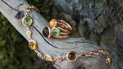 Drei Bouton Ringe von Tamara Comolli in Rosegold mit je einem Farbstein in orange, gruen und braun und dazu passendes Bouton-Armband auf Holzast drapiert