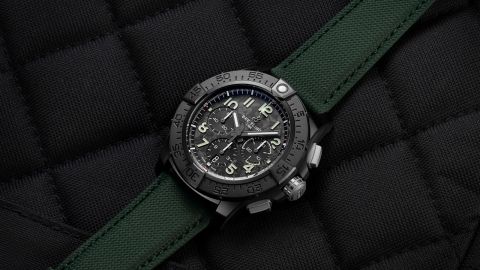 Breitling Avenger Chronograph Night Mission mit scharzem Keramikgehaeuse, schwarzem Zifferblatt und dunkelgruenem Textilband auf schwarzem gesteppten Stoffhintergrund liegend