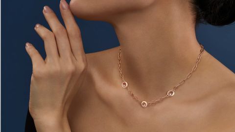 Weibliches Model vor blauem Hintergrun traegt ein Happy Diamonds Collier von Chopard in Rosegold mit drei runden Elementen mit je einem beweglichen Diamanten